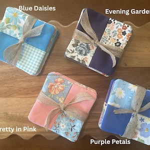 May include: Four sets of square fabric coasters tied with jute twine. The sets are labeled Blue Daisies with blue and gingham patterns, Evening Garden with floral and dark purple fabric, Pretty in Pink with floral and pink fabric, and Purple Petals with floral and blue fabric.