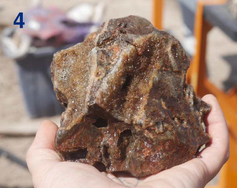 May include: A rough, irregular rock specimen featuring a deep brown and reddish-brown colour palette with crystalline, sparkling mineral deposits embedded within its crevices and along the textured, jagged surface of the stone formation.