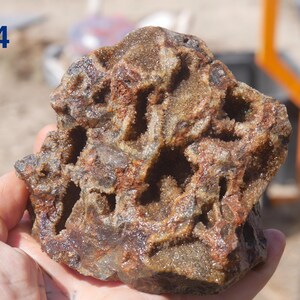 May include: A rough, porous rock specimen featuring a complex network of hollow cavities and jagged, crystalline interior surfaces. The exterior displays a mix of earthy brown, rust-red, and dark grey tones with a coarse, granular texture throughout.