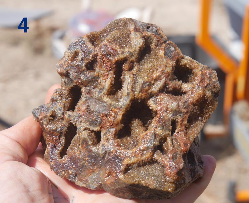 May include: A rough, porous rock specimen featuring a complex network of hollow cavities and jagged, crystalline interior surfaces. The exterior displays a mix of earthy brown, rust-red, and dark grey tones with a coarse, granular texture throughout.