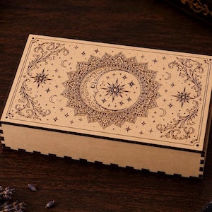 May include: A rectangular wooden box featuring a laser-engraved design on the lid. The artwork displays a central sun and crescent moon motif surrounded by intricate mandala patterns, stars, and swirling floral filigree in dark brown ink.