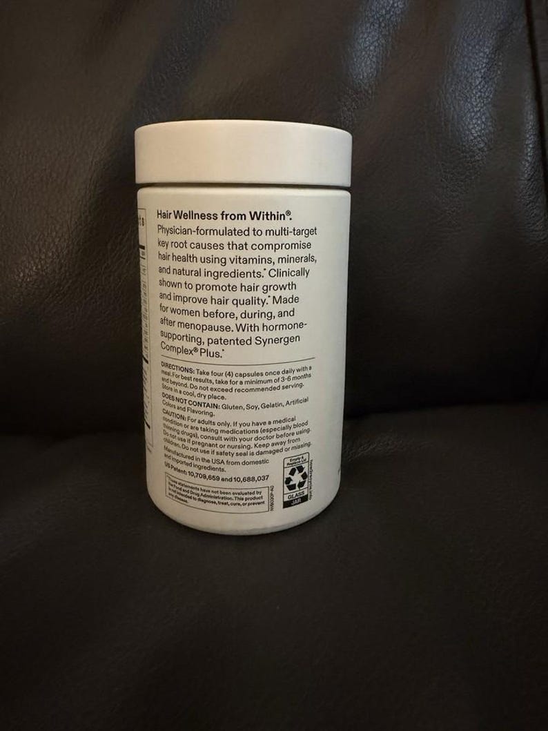 May include: A white cylindrical supplement bottle with a white screw-top lid. The label features black text detailing Hair Wellness from Within, physician-formulated ingredients, dosage instructions, and safety warnings for this dietary product.