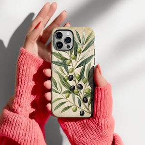 May include: A rectangular smartphone case featuring a botanical illustration of olive branches with green and black olives against a cream-colored background. The case has a cutout for a triple-lens camera system on the upper left corner.