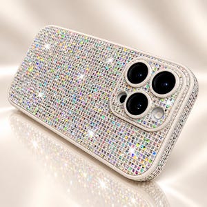 Könnte beinhalten: Eine Smartphone-Hülle, die mit kleinen, reflektierenden, mehrfarbigen quadratischen Kristallen bedeckt ist, die einen schimmernden, irisierenden Effekt erzeugen. Die Hülle hat einen erhöhten quadratischen Kameraausschnitt mit drei Linsen.