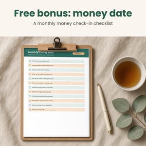 May include: A wooden clipboard holding a Monthly money date checklist with alternating light blue and peach rows, featuring a white pen and a small cup of tea nearby. The text reads Free bonus: money date, A monthly money check-in checklist.