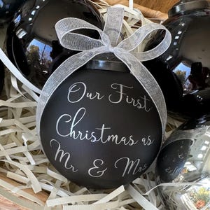 May include: Black Christmas ornament with a silver ribbon and the text "Our First Christmas as Mr & Mrs" written in silver lettering.