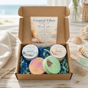 Puede incluir: Una caja de regalo de cartón que contiene dos recipientes redondos de exfoliante corporal etiquetados Coastal Vibes Soap Co. Seaside Spa y Golden Sands, además de dos jabones redondos en color melocotón y verde, con una tarjeta de agradecimiento.