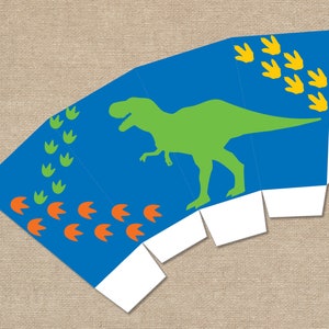 Könnte beinhalten: Eine blaue Party-Geschenkbox mit einer grünen Dinosauriersilhouette, orangefarbenen und grünen Dinosaurierspuren und gelben Fußabdrücken. Die Box ist gefaltet und bereit zum Zusammenbauen.