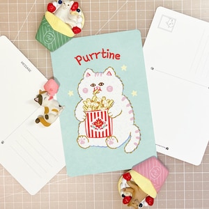 Peut inclure: Une carte postale bleu clair illustrée d'un chat blanc mangeant des frites avec le texte Purrtine, accompagnée de deux cartes postales vierges lignées et de deux figurines de chat dans des emballages de crêpes avec des fruits.