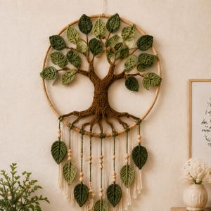 May include: A circular wall hanging featuring a crocheted brown tree with roots and various shades of green crocheted leaves inside a bamboo hoop. Below the hoop, several strands of white cord hang down, decorated with wooden beads and leaves.