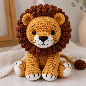 Può includere: Un leone di peluche all'uncinetto con corpo giallo dorato, una folta criniera marrone scuro testurizzata e occhi di sicurezza neri. Il leone ha un muso bianco con naso e bocca ricamati in nero, zampe bianche con artigli neri e una lunga coda.