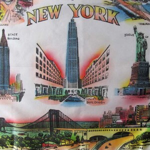 May include: White fabric featuring colorful illustrations of New York City landmarks. The design includes the Empire State Building, the Statue of Liberty, and the RCA Building, with the text "NEW YORK" at the top.