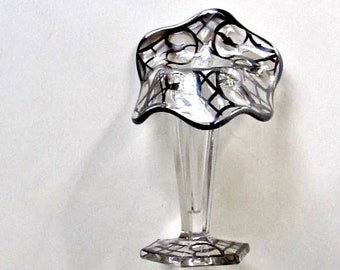 May include: A clear glass bud vase with a flared, scalloped top and a geometric base. The top and base feature a black, web-like design. The vase has a slender stem and is suitable for displaying a single flower or small bouquet.