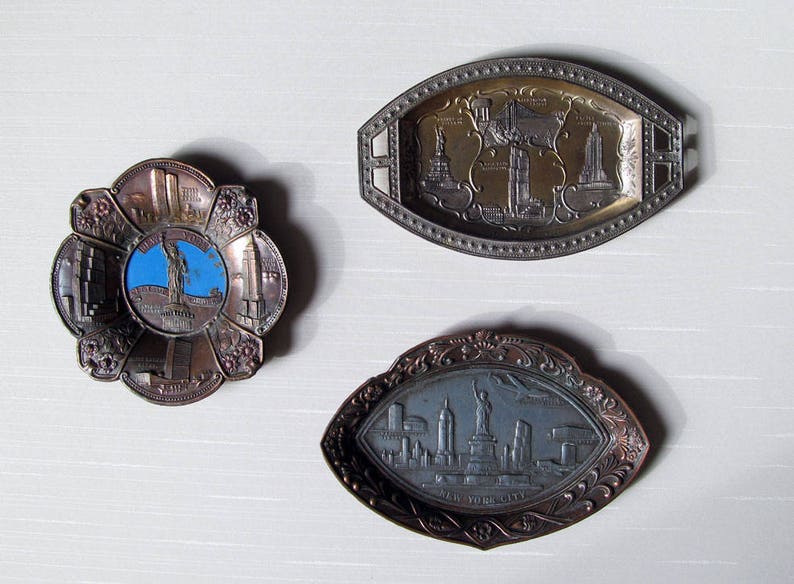 Puede incluir: Tres bandejas de metal vintage con dise&ntilde;os en relieve. Una es una bandeja redonda con forma de flor con un centro azul que representa la Estatua de la Libertad. Otra es una bandeja ovalada con monumentos de la ciudad. La tercera es una bandeja en forma de hoja con el horizonte de Nueva York.