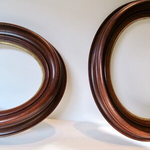 May include: Two oval picture frames with a dark brown, glossy finish. The frames have a decorative, ridged edge and a gold-colored inner rim. The frames are set against a white background.