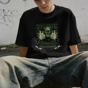 May include: A black short-sleeve t-shirt featuring a green graphic of Frankenstein's monster surrounded by flames. The text reads "THE MOST WONDERFUL TIME OF THE YEAR," "HALLOWEEN," "FOREVER," and "HALLOWEEN" repeated in a small block at the bottom.