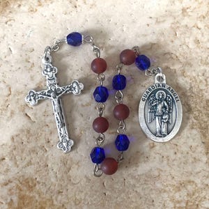 May include: A silver rosary with blue and brown beads. The rosary has a silver crucifix and a silver charm with the words "Guardian Angel".