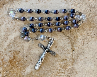 May include: A silver rosary with purple and black beads and a silver crucifix.