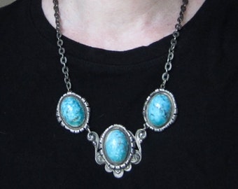 May include: A silver chain necklace with three turquoise stones set in silver. The stones are oval shaped and have a light blue color.
