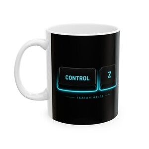 May include: A white ceramic mug featuring a black graphic design on the front. The design displays two black computer keyboard keys labeled CONTROL and Z with a glowing blue outline. Below the keys, the text reads ISAIAH 43:25 in blue.