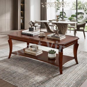 May include: A rectangular wooden coffee table with a rich brown finish, featuring curved legs and a lower storage shelf. The top surface holds two stacks of books, a small white cup, and a decorative object. A potted succulent sits on the lower shelf.
