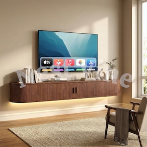 May include: A wall-mounted, walnut-colored wooden media console with a slatted front design and integrated under-cabinet lighting. The console features two central doors and is topped with books, decorative objects, and a flat-screen television.