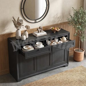 May include: A black wooden sideboard featuring two open drawers filled with white ceramic plates, bowls, and mugs, along with a teapot. The top surface holds two vases with dried botanicals, a stack of books, and a wooden bowl of fruit.