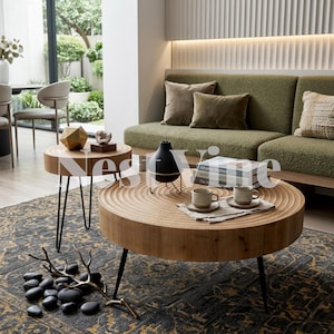 May include: Two round wooden coffee tables with concentric ring carvings on the surface and thin black metal legs. The larger table holds a black vase, two ceramic mugs on a cloth, and books. A decorative branch and stones sit on the rug.