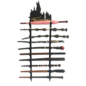 May include: A black wall-mounted display rack featuring a silhouette of a castle and the gold text Ollivanders. The rack holds ten various wands of different shapes, colours, and textures, including brown, black, silver, and a pink umbrella-shaped wand.
