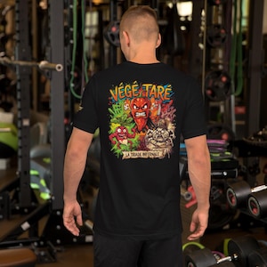 May include: A black short-sleeved t-shirt featuring a colorful graphic on the back. The design displays three cartoon vegetables with angry expressions, the text "VÉGÉ TARÉ" at the top, and the text "LA TRIADE INFERNALE" on a banner at the bottom.
