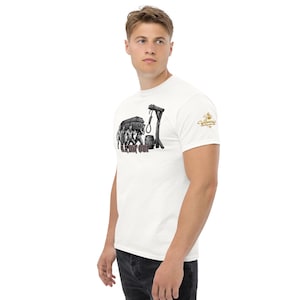 May include: A white short-sleeve t-shirt featuring a black and white graphic of four figures carrying a coffin toward a gallows with a noose and a barrel. The text "LE DIT OUI" is printed in red below the graphic, and a gold logo is on the sleeve.