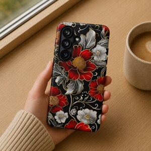 May include: A black smartphone case featuring a detailed floral pattern with vibrant red and white flowers, gold-colored centers, and silver-toned leaves. The design includes delicate white swirling vines and dots against a solid black background, with a cutout for the camera lens array.