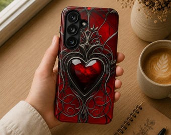 Könnte beinhalten: Eine Smartphone-Hülle mit tiefrotem Hintergrund und einem glänzenden Herz-Emblem in der Mitte. Das Design zeigt komplizierte, silberfarbene Filigranmuster, die sich um das Herz winden und einen komplexen, geschichteten Effekt erzeugen.