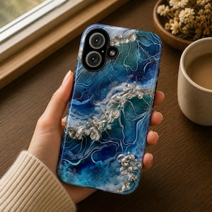 May include: A smartphone case featuring a swirling blue and teal marbled resin design with embedded silver-toned metallic floral accents. The surface has a glossy finish with visible depth and texture, surrounding a dual-lens camera cutout.