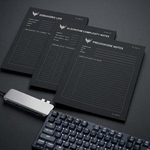May include: Three black paper pads with white text and lines, labeled Debugging Log, Algorithm Complexity Notes, and Pseudocode Notes. Each pad features a small logo at the top, a silver USB-C hub, and a mechanical keyboard with backlit keys.