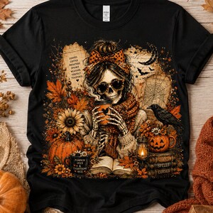 May include: A black t-shirt featuring a graphic of a skeleton wearing a polka dot bow and sunglasses, holding a coffee cup. The design includes autumn leaves, a pumpkin, a crow, a lantern, books, and text reading LEAVES COFFEE SWEATERS SPOOKY WEATHER PERFECT TOGETHER.