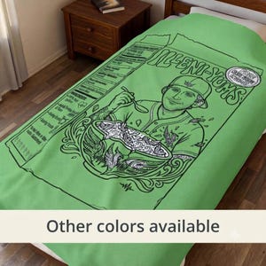 May include: A light green fleece blanket featuring a black line art graphic of a cereal box labeled Illeni-Yums. The design includes a person wearing a baseball cap eating from a bowl, with nutritional facts and text printed on the side.
