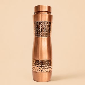 May include: A cylindrical copper water bottle with a smooth finish and two distinct bands of hammered, textured detailing. The bottle features a matching screw-top lid and a slightly tapered neck, showcasing a metallic, reddish-brown hue throughout.