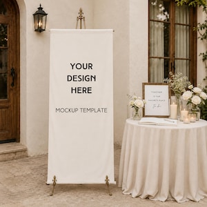 May include: A vertical white fabric banner on a metal stand featuring the black text YOUR DESIGN HERE MOCKUP TEMPLATE. Beside it, a round table with a beige tablecloth holds a framed sign, white flowers in vases, candles, and a notebook.