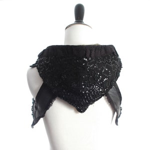 May include: A black sequined and lace hooded vest with leather straps. The vest is displayed on a white mannequin.