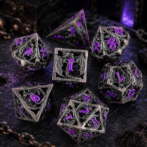 May include: A set of seven polyhedral dice featuring a metallic silver finish with intricate dragon-themed cutouts and vibrant purple numbers. The dice set includes various geometric shapes, each displaying detailed dragon wings and scales in relief.