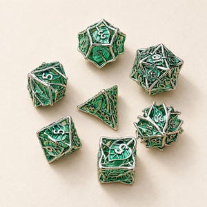 May include: A set of seven polyhedral dice featuring a silver metal cage design with intricate leaf patterns and vibrant green enamel inlay. Each die displays clear, embossed numbers, including a d20, d12, d10, d8, d6, d4, and a percentile die.
