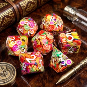 May include: A set of seven polyhedral dice made of clear resin filled with colorful miniature fruit slices. Each die features bold white numbers. The collection includes various shapes such as a d20, d12, d10, d8, d6, and d4, all displaying vibrant citrus and berry patterns.