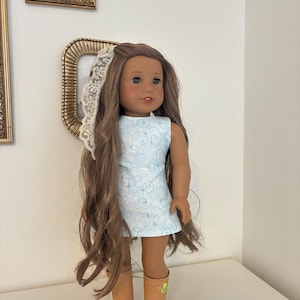 Puede incluir: Una mu&ntilde;eca con cabello largo casta&ntilde;o, vestida con un vestido sin mangas azul claro con un patr&oacute;n de remolinos blancos y peque&ntilde;as estrellas. La mu&ntilde;eca lleva un accesorio de encaje blanco en el cabello y botas color canela con un detalle verde.