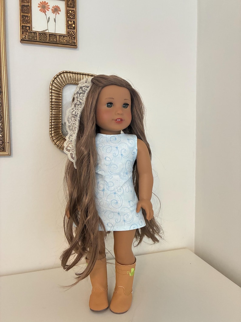 Puede incluir: Una mu&ntilde;eca con cabello largo casta&ntilde;o, vestida con un vestido sin mangas azul claro con un patr&oacute;n de remolinos blancos y peque&ntilde;as estrellas. La mu&ntilde;eca lleva un accesorio de encaje blanco en el cabello y botas color canela con un detalle verde.