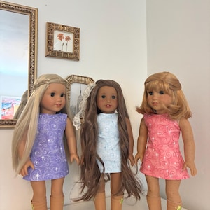 Puede incluir: Tres mu&ntilde;ecas de pie una al lado de la otra, cada una con un vestido sin mangas con un patr&oacute;n de remolinos y detalles de estrellas. La mu&ntilde;eca de la izquierda tiene el pelo largo y rubio, la del centro tiene el pelo largo y casta&ntilde;o, y la de la derecha tiene el pelo casta&ntilde;o rojizo hasta los hombros. Las tres llevan botas de color tostado.