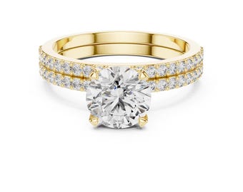 May include: A yellow gold ring featuring a large round brilliant-cut center stone held by four prongs. The band is split into two rows, each encrusted with a series of small, round, clear pavé-set stones that extend along the sides of the ring.
