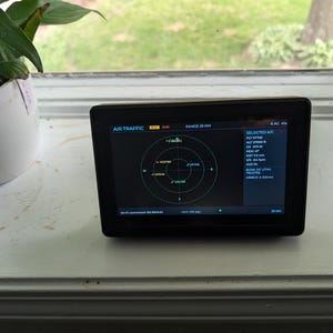 May include: A black rectangular digital air traffic monitor displaying a circular radar screen with flight data, including altitude, heading, and distance, with the text AIR TRAFFIC and RANGE 25 NM visible at the top of the illuminated screen interface.