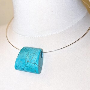 May include: A turquoise pendant with dark brown veining suspended on a thin silver-toned metal wire collar necklace. The pendant has a smooth, curved, rectangular shape with a hole on the right side for the wire to pass through.