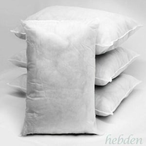 May include: A stack of four rectangular white pillow inserts. Each pillow insert is made of a plain, smooth, non-woven fabric casing filled with soft material, creating a plump and uniform appearance for each individual cushion form.